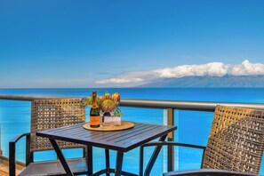 A balcony with wicker chairs, a wooden table, a bottle of champagne, and a vase with flowers. - Sands of Kahana Resort by KBM (Lahaina)