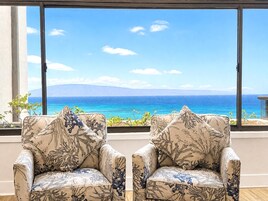 A room with two armchairs facing a large window overlooking a coastal view.
