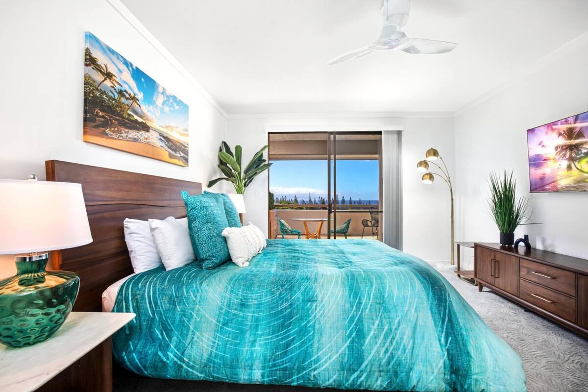 A bedroom with a bed, a nightstand, a lamp, a dresser, a balcony with a view, and a ceiling fan.