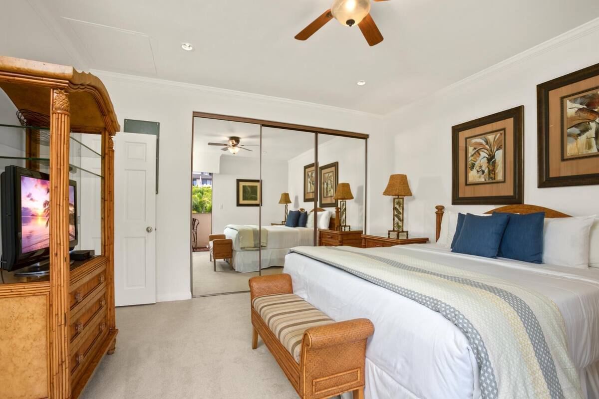 A bedroom with a bed, bedside tables, a mirror, a television, and a ceiling fan.