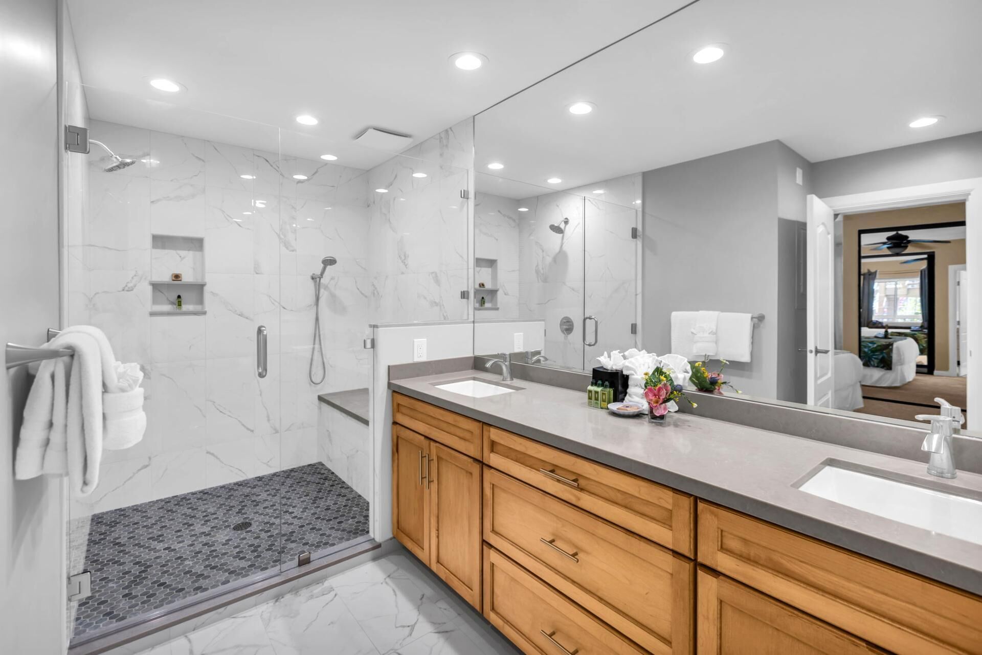 Une salle de bain moderne avec un grand miroir, deux vasques, des meubles en bois et un espace douche.