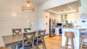 Una cocina moderna con armarios blancos, un refrigerador de acero inoxidable y una mesa de comedor de madera con sillas.
