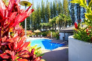Relax by the serene pool surrounded by lush tropical vegetation and shaded by a thatched umbrella.