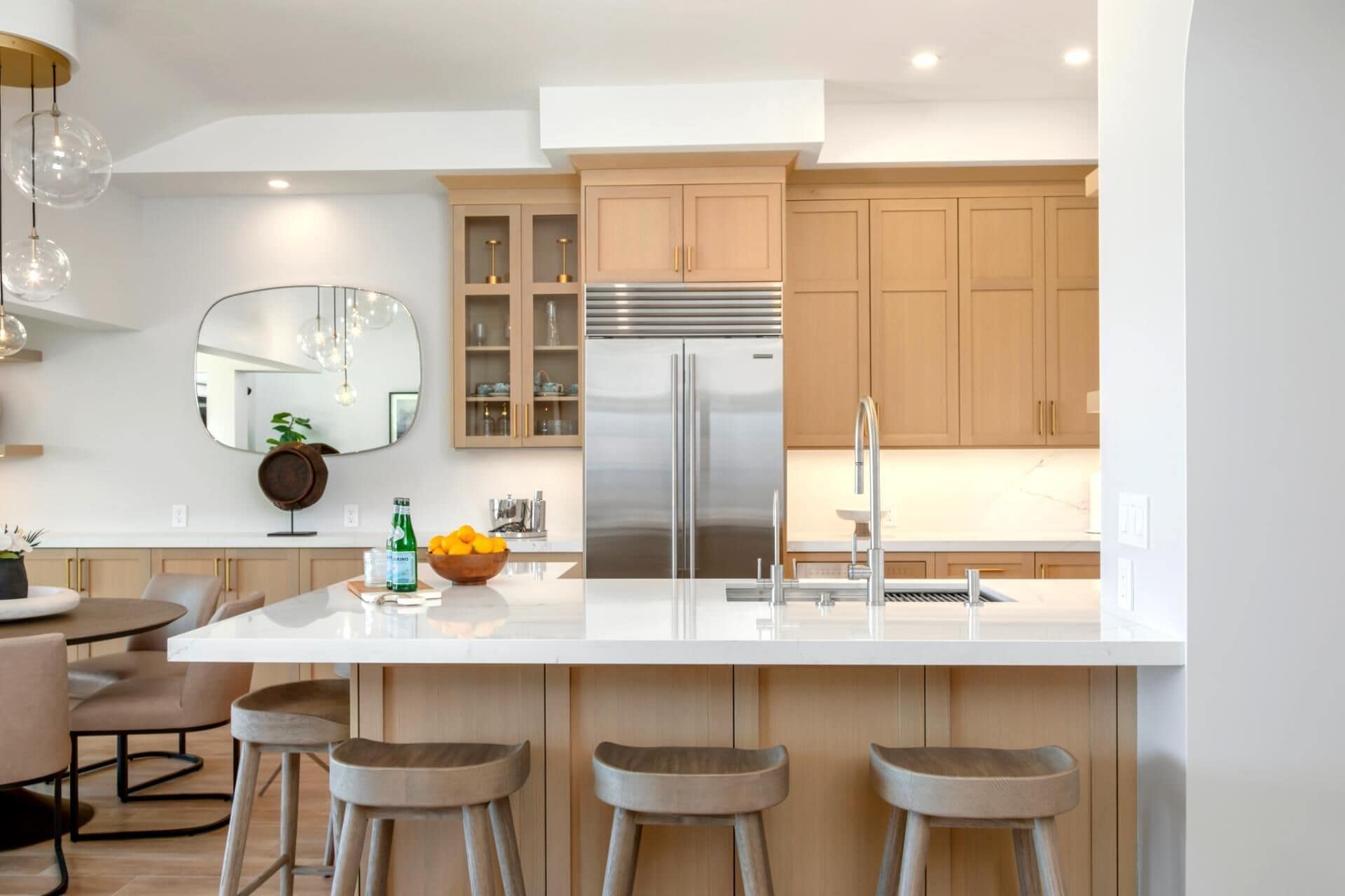 Une cuisine moderne dotée d’un îlot central, d’appareils électroménagers en acier inoxydable, de meubles de rangement en bois et d’un coin bar avec des tabourets.