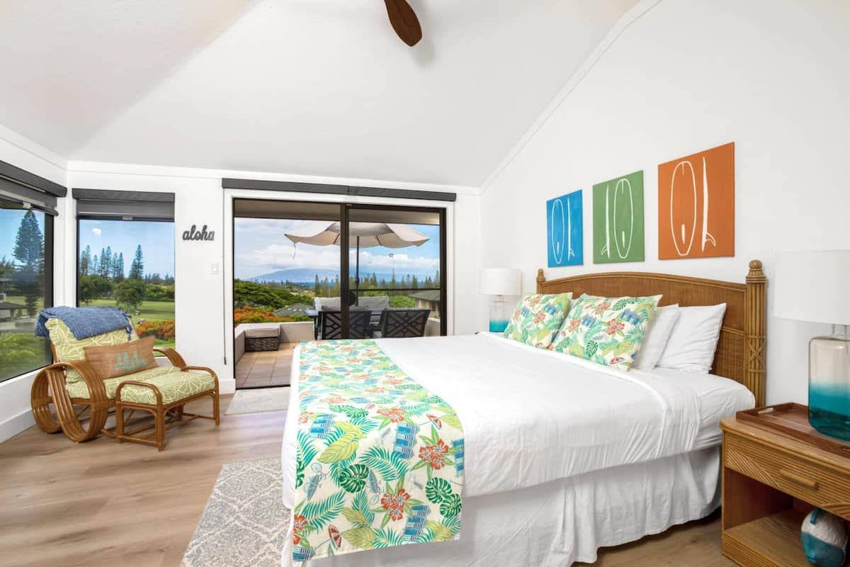 A spacious bedroom with a large bed, a balcony with a table and chairs, and a view of the outdoors.