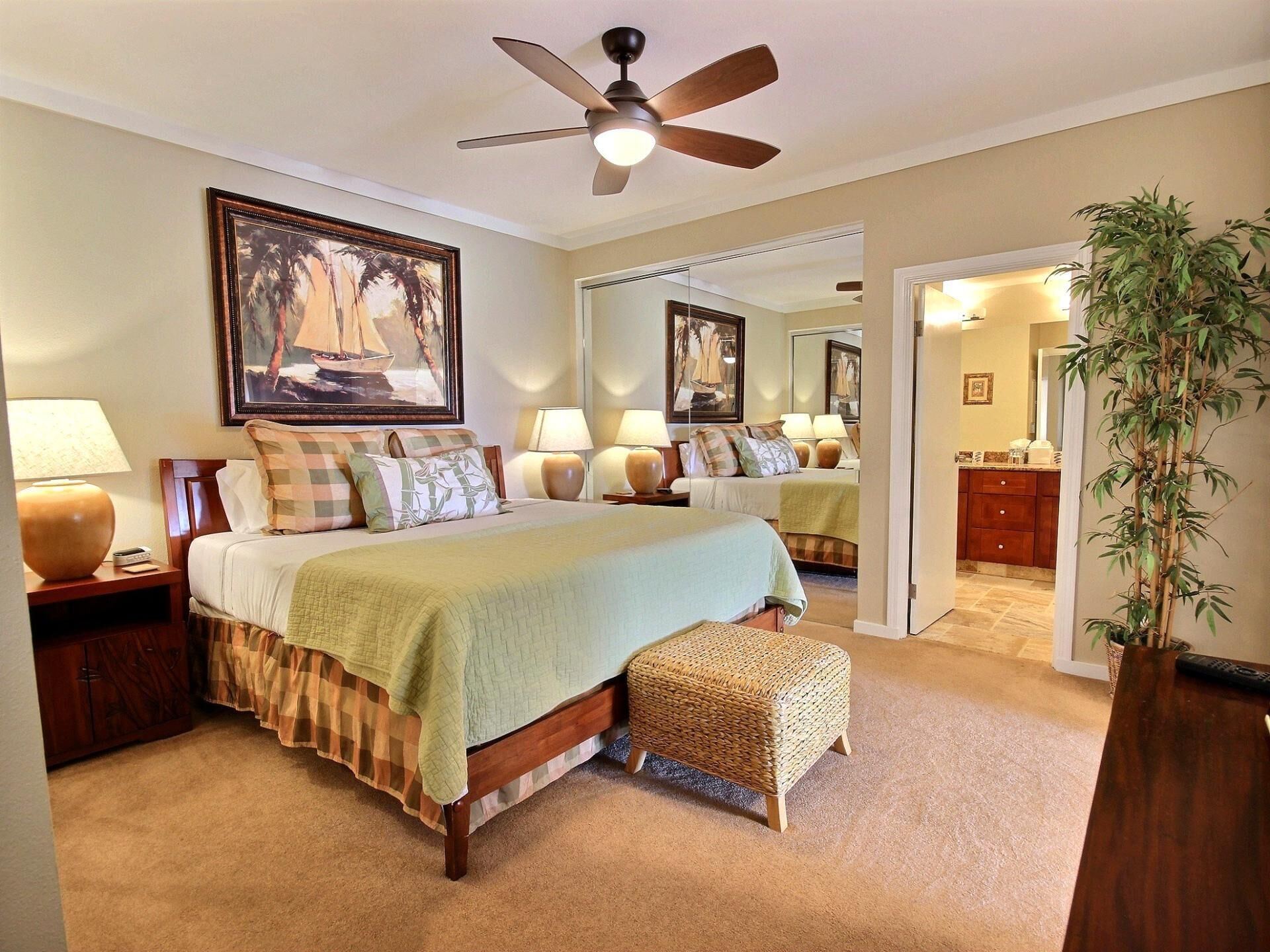 A bedroom with a bed, bedside tables, lamps, a ceiling fan, a large mirror, and a potted plant.