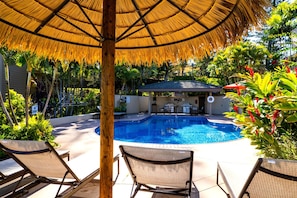 Relax by the clear pool surrounded by lush greenery and lounge chairs.