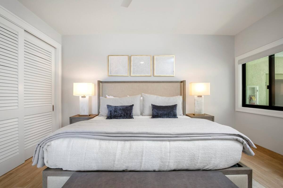 A neatly made bed with a headboard, two bedside lamps, and three framed artworks above it.