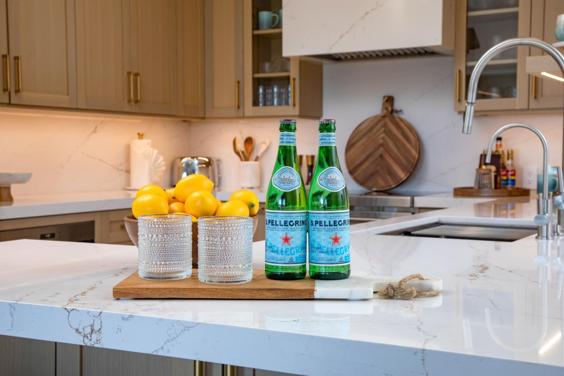 Un piano di lavoro in cucina con limoni, due bottiglie di acqua frizzante Pellegrino e un tagliere di legno.