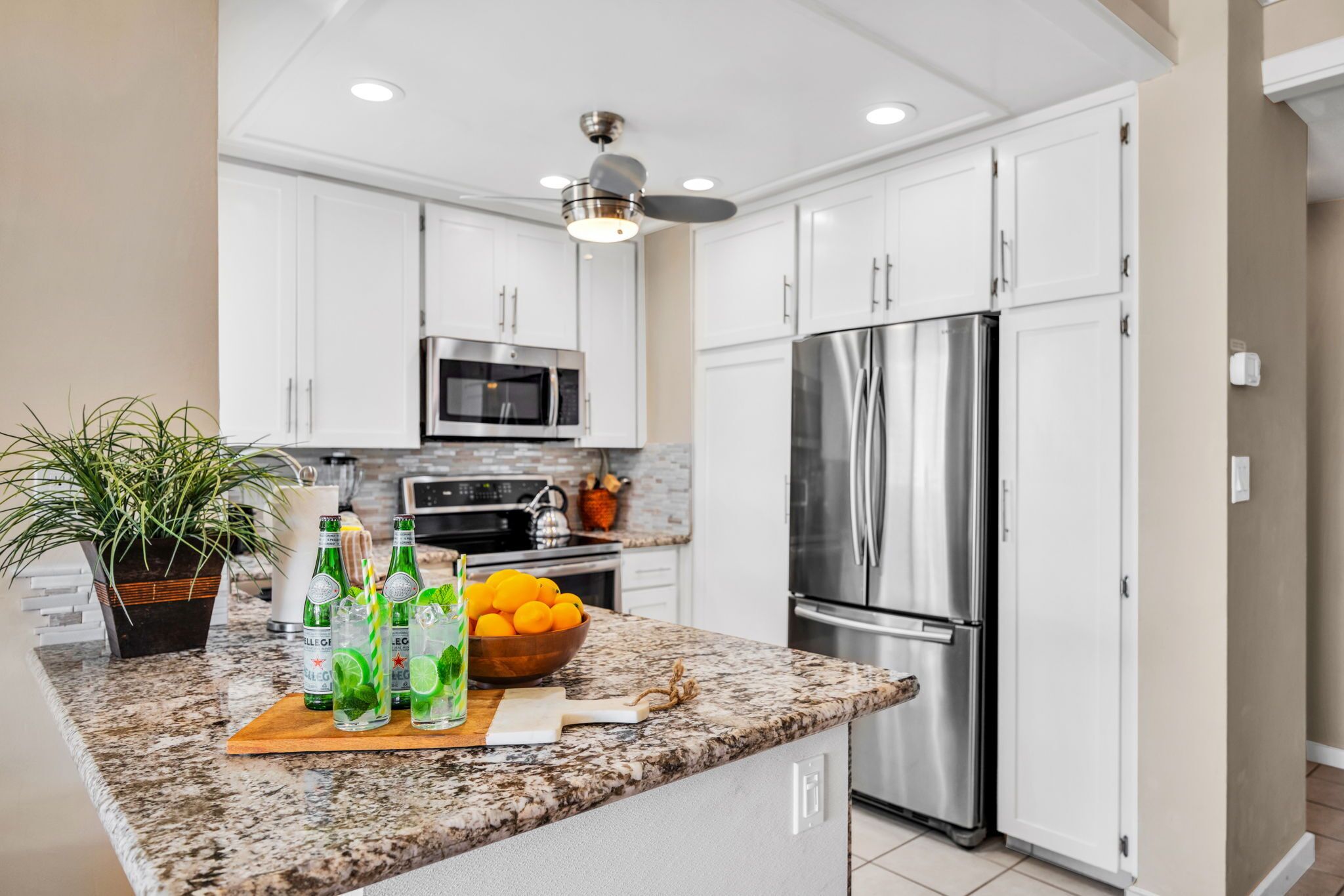 Una cocina moderna con gabinetes blancos, electrodomésticos de acero inoxidable, encimera de granito y ventilador de techo.