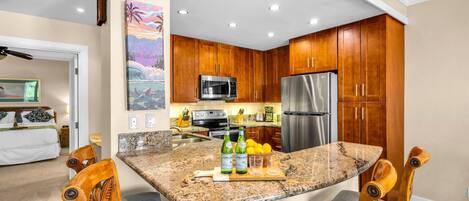 A modern kitchen with granite countertops, wooden cabinets, stainless steel appliances, and a dining area with wooden chairs.