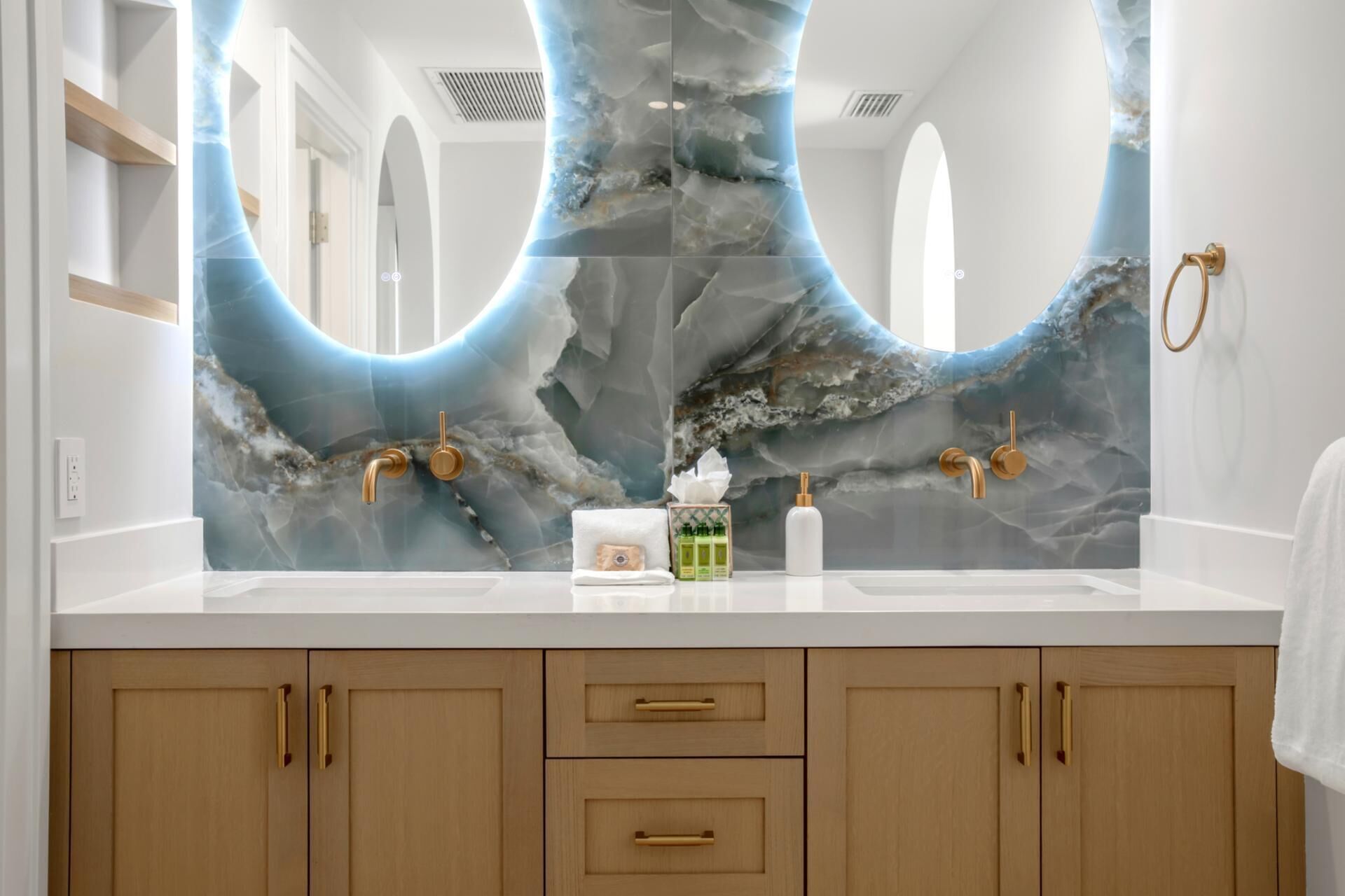 A bathroom with a marble backsplash, gold faucets, and wooden cabinets.