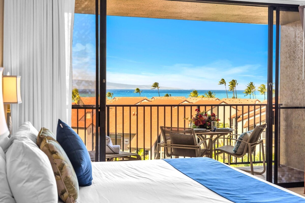 A hotel room with a balcony, a bed, a table with chairs, and a view of the beach.