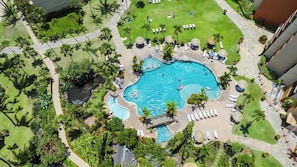 A large pool surrounded by palm trees and lounge chairs, with a stone pathway leading to the pool.