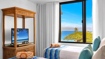 A hotel room with a large window offering a view of a tropical beach and palm trees.