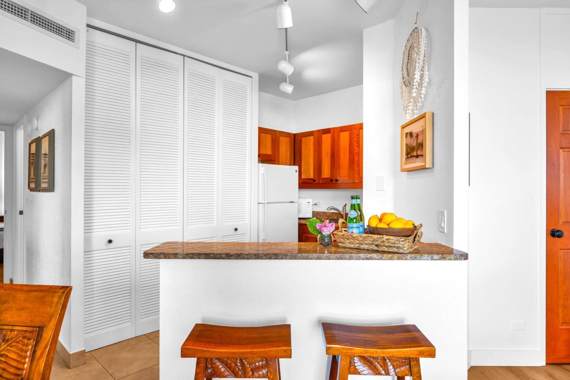 A kitchen with wooden cabinets, a white countertop, and two wooden stools.