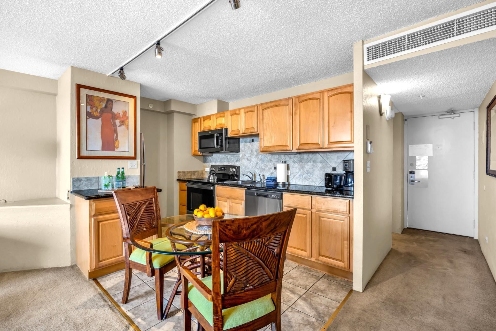 Cocina compacta con armarios de madera, microondas, cafetera y comedor con sillas y mesa.