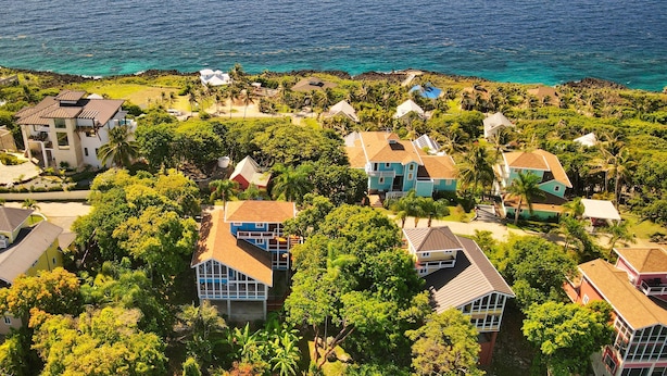 A coastal residential area with houses surrounded by lush greenery and a view of the ocean. - Incredible Ocean views from both sides of this hill top home. (Roatan)
