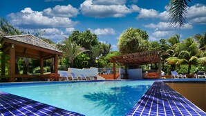 A swimming pool with blue tiled edges, lounge chairs, and a covered area with a tiled roof. - Incredible Ocean views from both sides of this hill top home. (Roatan)