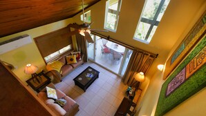 A spacious living area with a high ceiling, a ceiling fan, a sofa set, a coffee table, and a dining area visible through a glass door. - Incredible Ocean views from both sides of this hill top home. (Roatan)