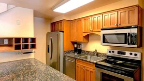 Eine Küche mit Granit Arbeitsplatten, Holzschränken, einem Edelstahlkühlschrank, einer Mikrowelle und einem Backofen.