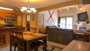 Ein Essbereich mit Holztisch und -stühlen, eine Küche mit Mikrowelle und Herd, ein Wohnbereich mit Sofa und Fernseher.