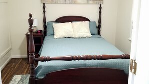 Een slaapkamer met een hemelbed van hout, een nachtkastje met een lamp en een aan de muur hangend schilderij.