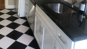 A kitchen with white cabinets, a black countertop, and a checkered floor. - Fisher Park condo on Elm St., new kitchen, 1 mile from downtown (Greensboro)