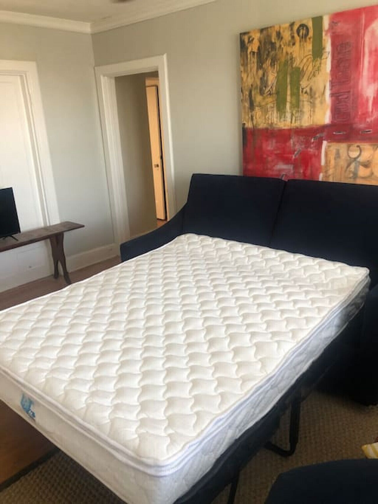 Een kamer met een groot bed, een televisie op een standaard en een schilderij aan de muur.