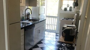 A narrow kitchen with a black and white checkered floor, white cabinets, and a window with blinds. - Fisher Park condo on Elm St., new kitchen, 1 mile from downtown (Greensboro)