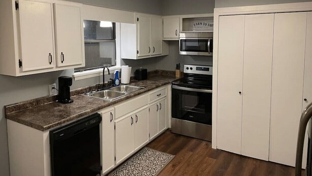 Una cocina compacta con gabinetes blancos, horno integrado, cafetera y lavavajillas.