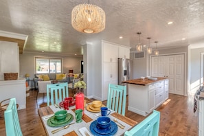 A modern kitchen with white cabinets, a wooden island, and a dining area with teal chairs and a wooden table set for four. - Mesa Manor: Comfortable & Modern Family Retreat (Fruita)