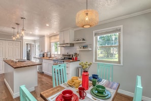 A modern kitchen with white cabinets, a wooden island, and a dining table set with colorful dishes. - Mesa Manor: Comfortable & Modern Family Retreat (Fruita)