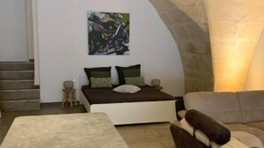 Een moderne woonkamer met een gebogen plafond, een bed met groen en wit beddengoed, een bank met bruine kussens en een bijzettafeltje met lades.
