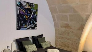 Een moderne slaapkamer met een wit bed, groene en zwarte kussens en een groot abstract schilderij aan de muur.