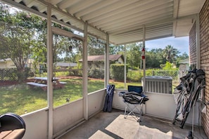 Une terrasse couverte avec de grandes fenêtres, une chaise pliante et un appareil de climatisation.