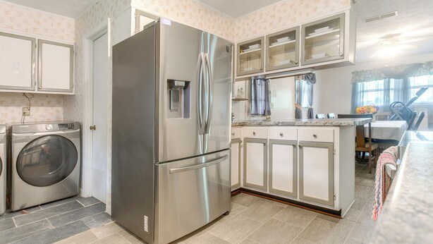 Una cocina con refrigerador de acero inoxidable, lavadora y comedor con mesa y sillas.