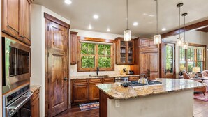 Una cucina moderna con mobili in legno, un piano di lavoro in granito, elettrodomestici in acciaio inossidabile e illuminazione a sospensione.