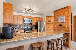 A kitchen with wooden cabinets, stainless steel appliances, a granite countertop, and a bar stool area.