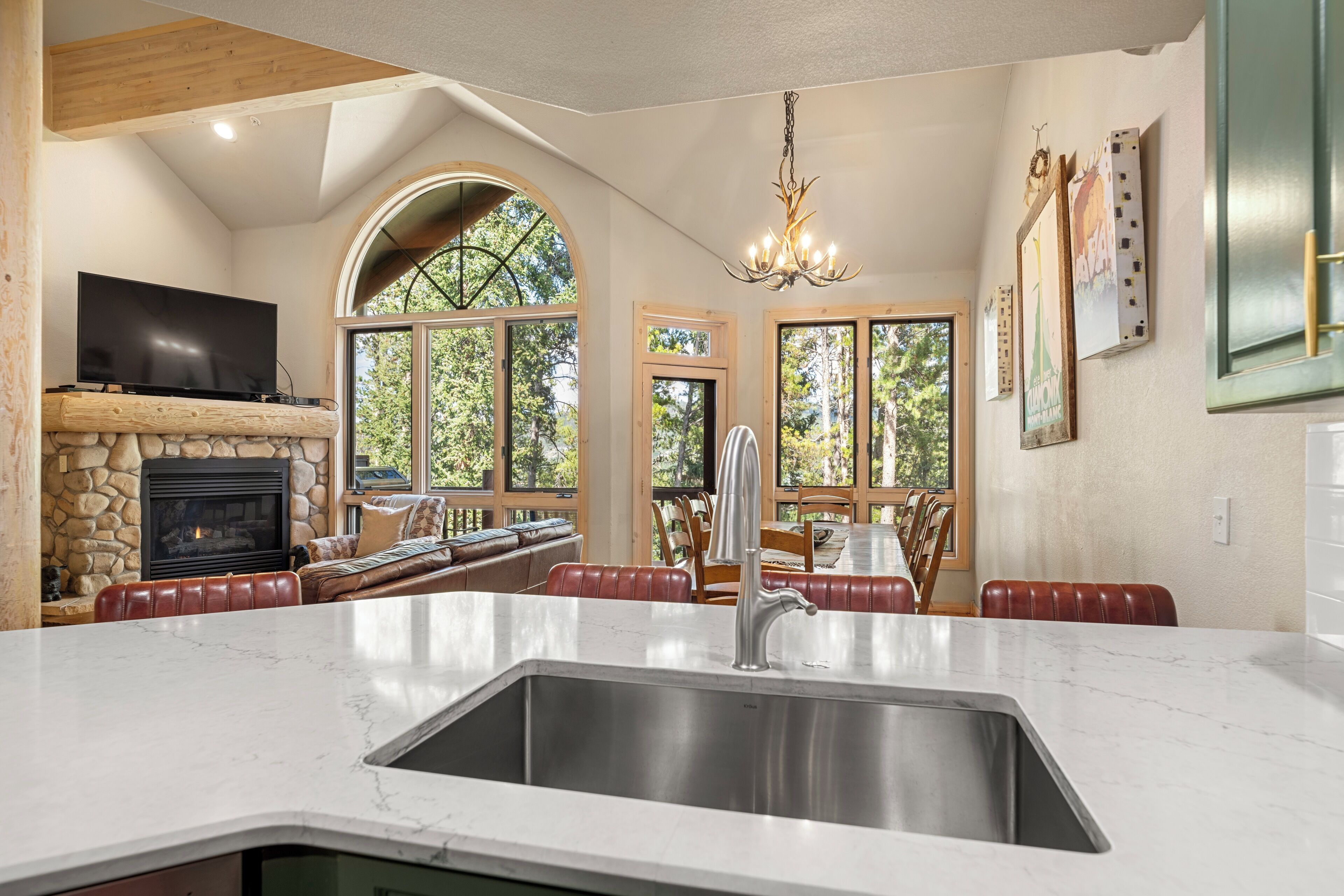A kitchen with a stone fireplace, a large island with a sink, and a dining area with red leather chairs.