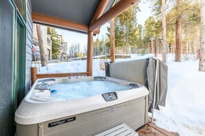 Un bain à remous doté d’une terrasse en bois, entouré de neige et d’arbres.