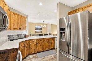 A modern kitchen with wooden cabinets, a stainless steel refrigerator, and a marble countertop.