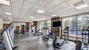A gym with various exercise equipment, large windows, and a stone wall. - Close to Peak 9, On Main St, Shared Pool/Hot Tubs. (Breckenridge)