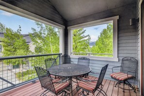 Een overdekt terras met een ronde tafel en stoelen, grote ramen en uitzicht op een woonwijk.
