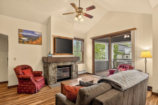 A living room with a fireplace, a red leather chair, a brown sofa, and a ceiling fan.