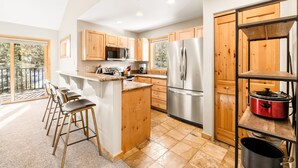 A modern kitchen with wooden cabinets, stainless steel appliances, and a bar area with stools.