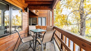 Una terraza de madera con una mesa y sillas, con vista a un árbol de hojas amarillas.