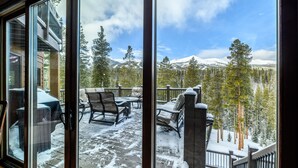 En snötäckt terrass med utemöbler, en trappa och utsikt över snöklädda berg och träd.