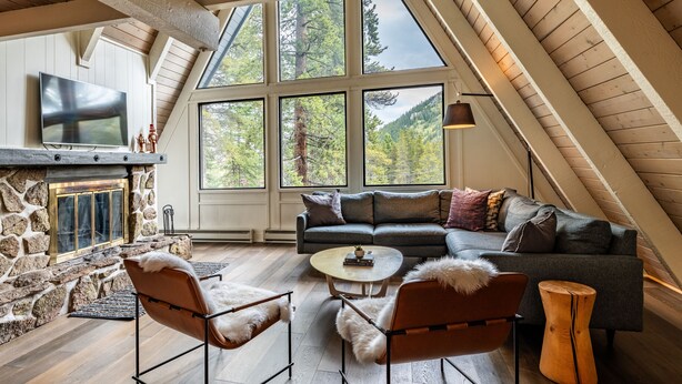 A cozy loft bedroom with a stone fireplace, large windows, a modern sofa, and a flat-screen TV. - Adventure Awaits! Cozy Aframe 5 Min to Breck. (Breckenridge)