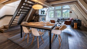 A spacious loft with a high ceiling, exposed wooden beams, a dining area with a long table and chairs, a staircase, and large windows offering views of the outdoors. - Adventure Awaits! Cozy Aframe 5 Min to Breck. (Breckenridge)